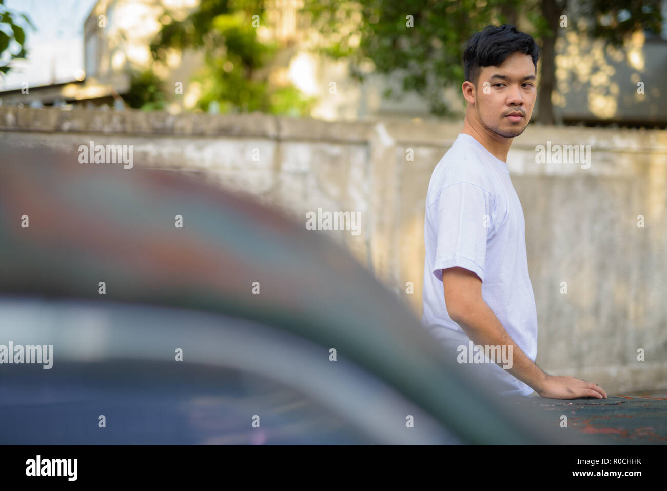 Junge asiatischer Mann mit rostigen alten Auto in den Straßen im Außenbereich Stockfoto