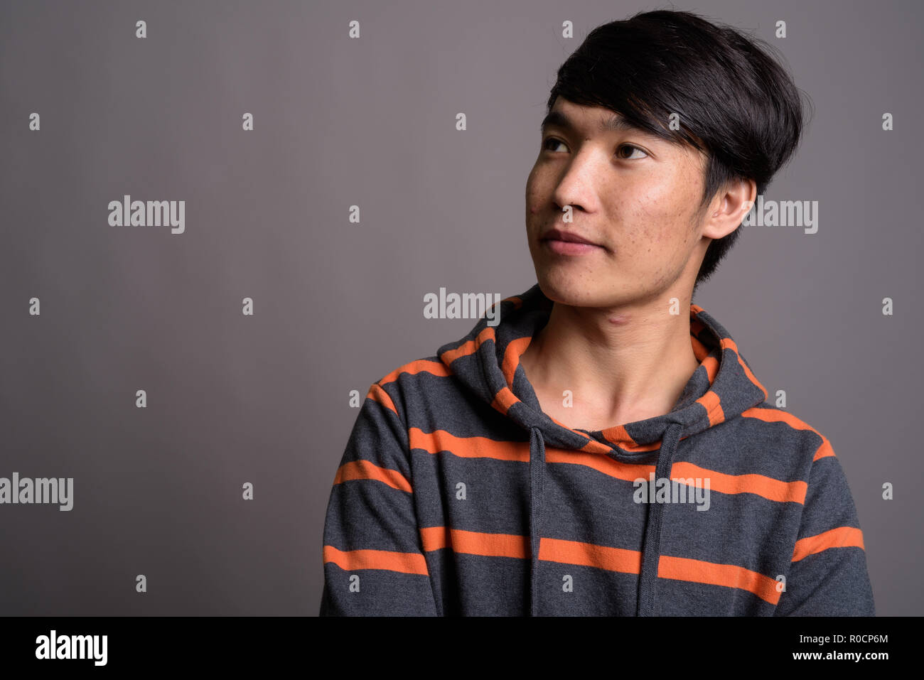 Jungen asiatischen Mann, der gestreifte Hoodie gegen grauer Hintergrund Stockfoto