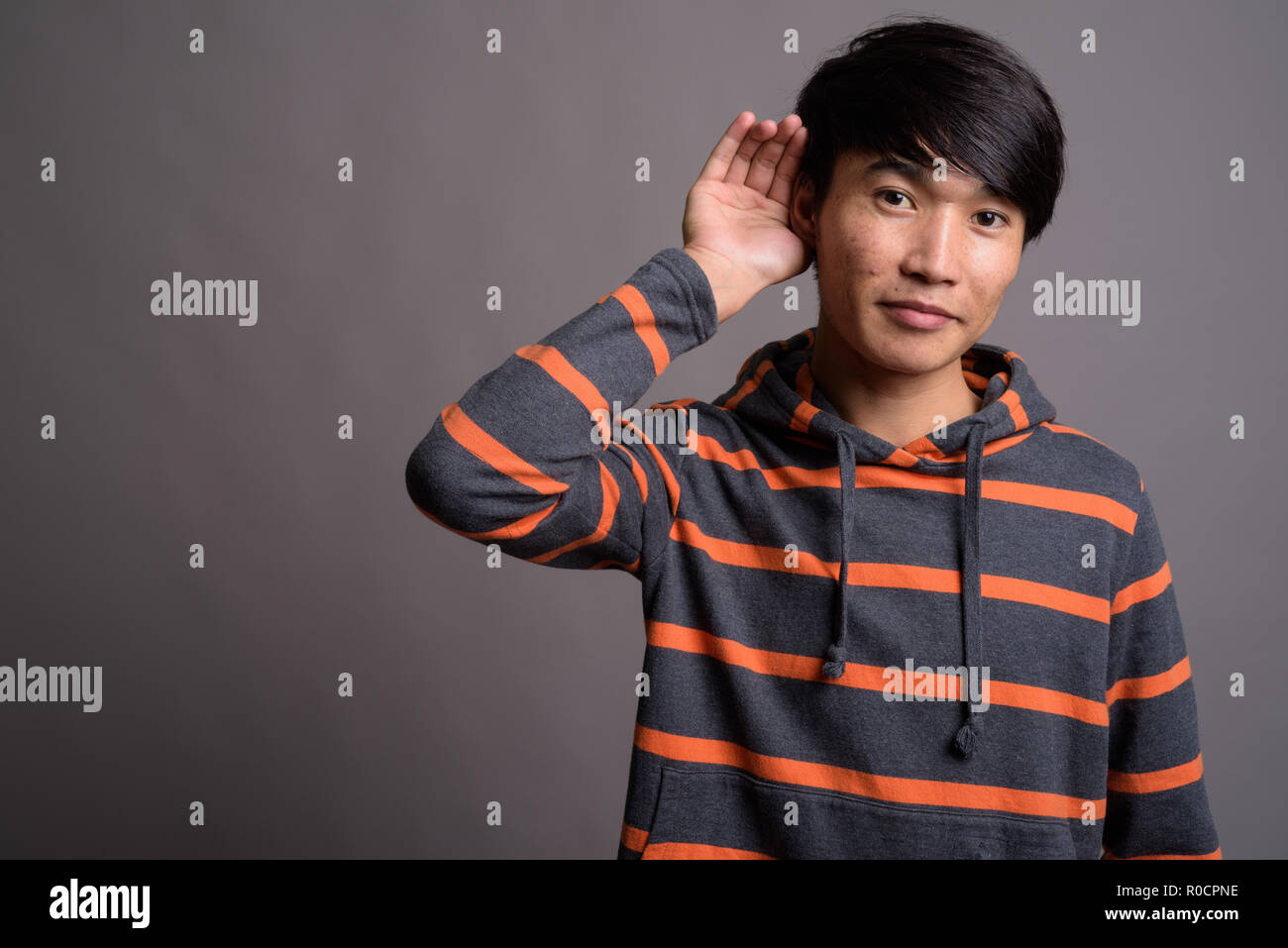 Jungen asiatischen Mann, der gestreifte Hoodie gegen grauer Hintergrund Stockfoto