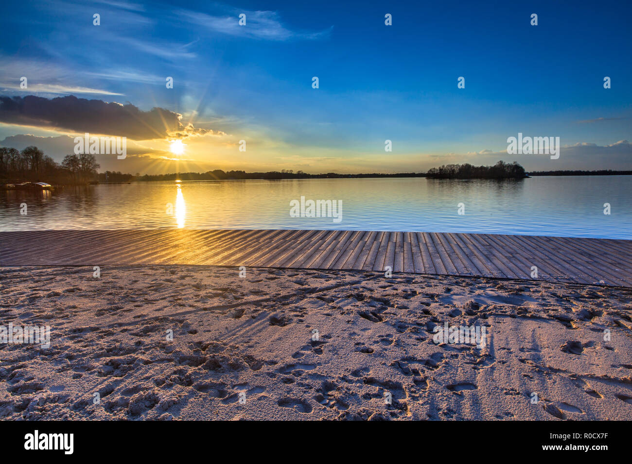 Holz- Freizeit Schwimmen deck und Sandstrand am See während der spektakulären Sonnenuntergang über dem Wasser Stockfoto
