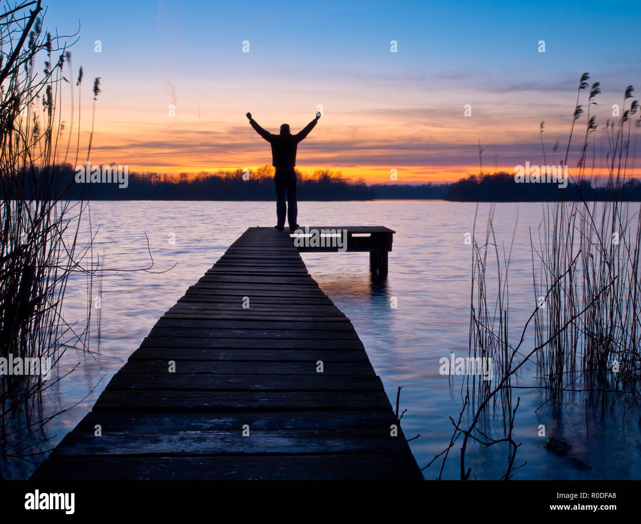 Mann auf einem Steg hebt seine Arme bei Sonnenuntergang Stockfoto