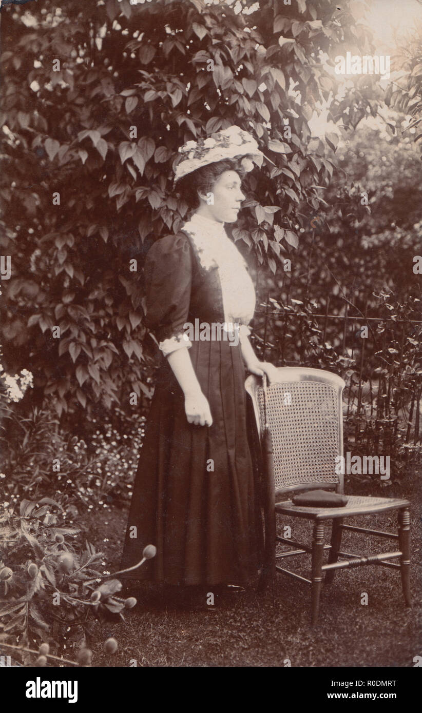 Jahrgang fotografische Postkarte von einem modischen Dame stand neben einem Stuhl in einem Garten Stockfoto