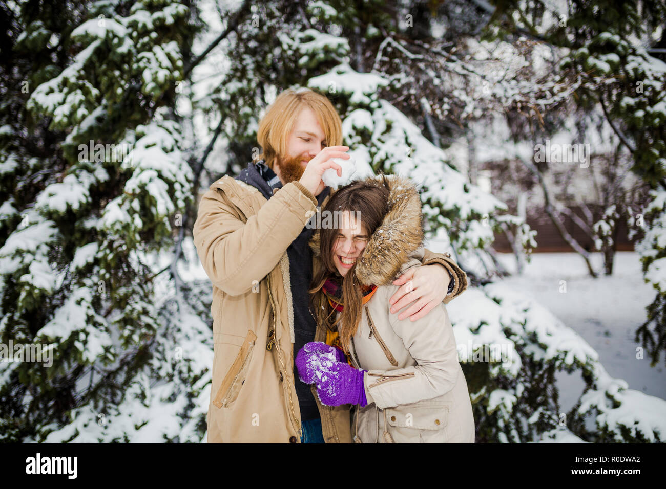 Junge kaukasier Junge mit Bart und ein Mädchen haben ein Datum im Freien im Winter Park vor dem Hintergrund eines schneebedeckten Nadelbaumbaum spielen Schneebälle, Thr Stockfoto