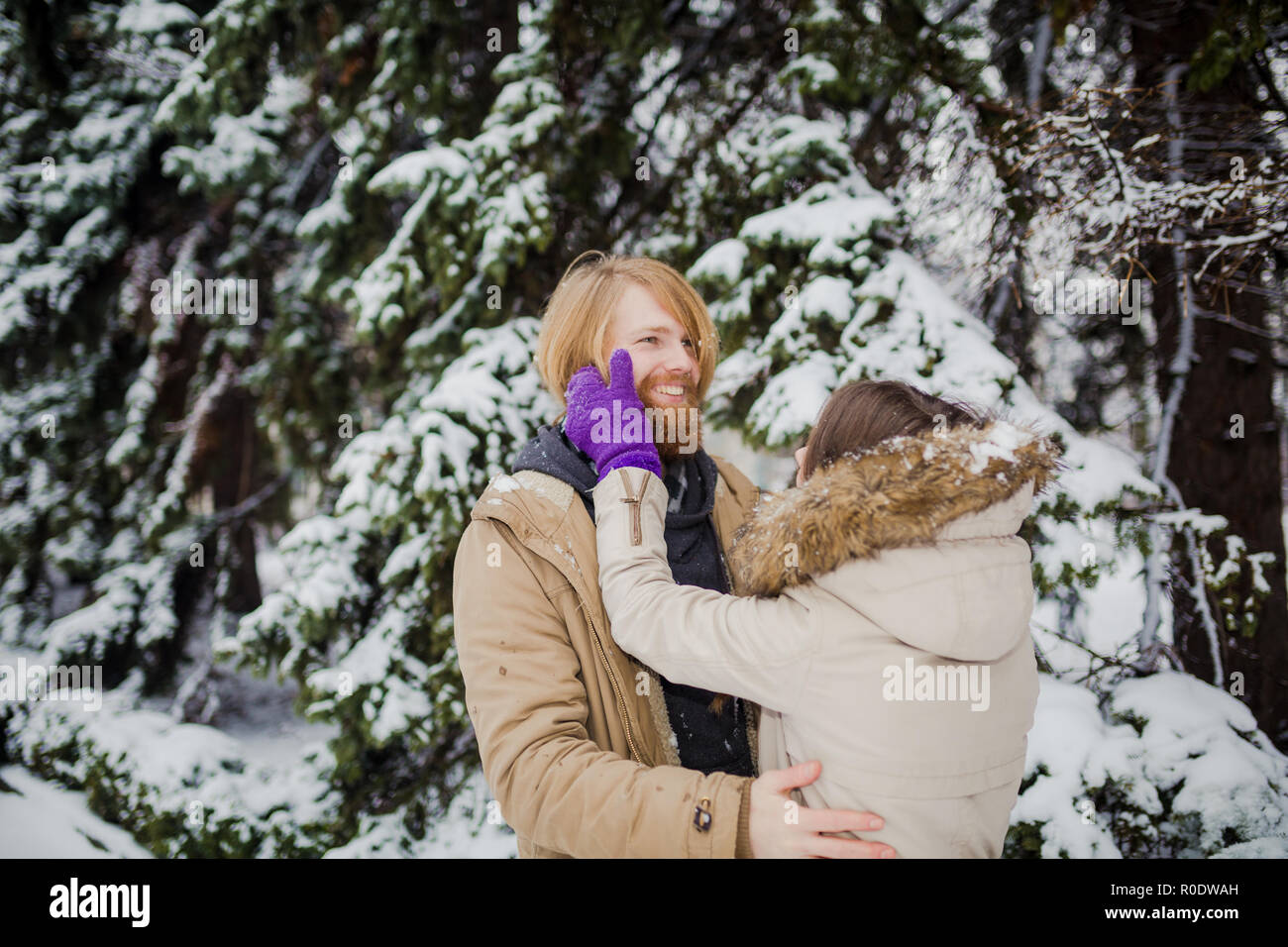 Junge kaukasier Junge mit Bart und ein Mädchen haben ein Datum im Freien im Winter Park vor dem Hintergrund eines schneebedeckten Nadelbaumbaum spielen Schneebälle, Thr Stockfoto