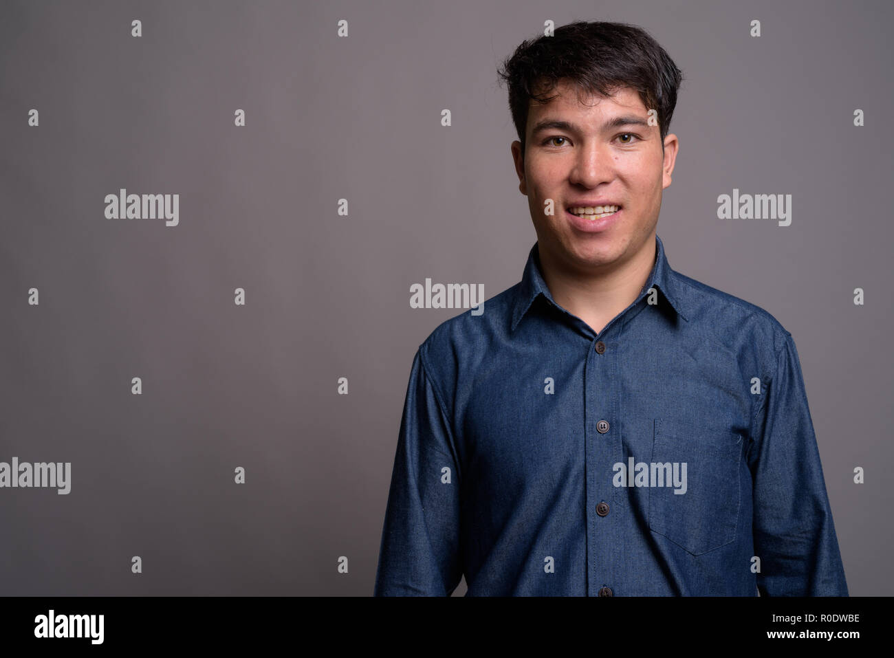 Jungen asiatischen Mann mit blauem Hemd gegen grauer Hintergrund Stockfoto