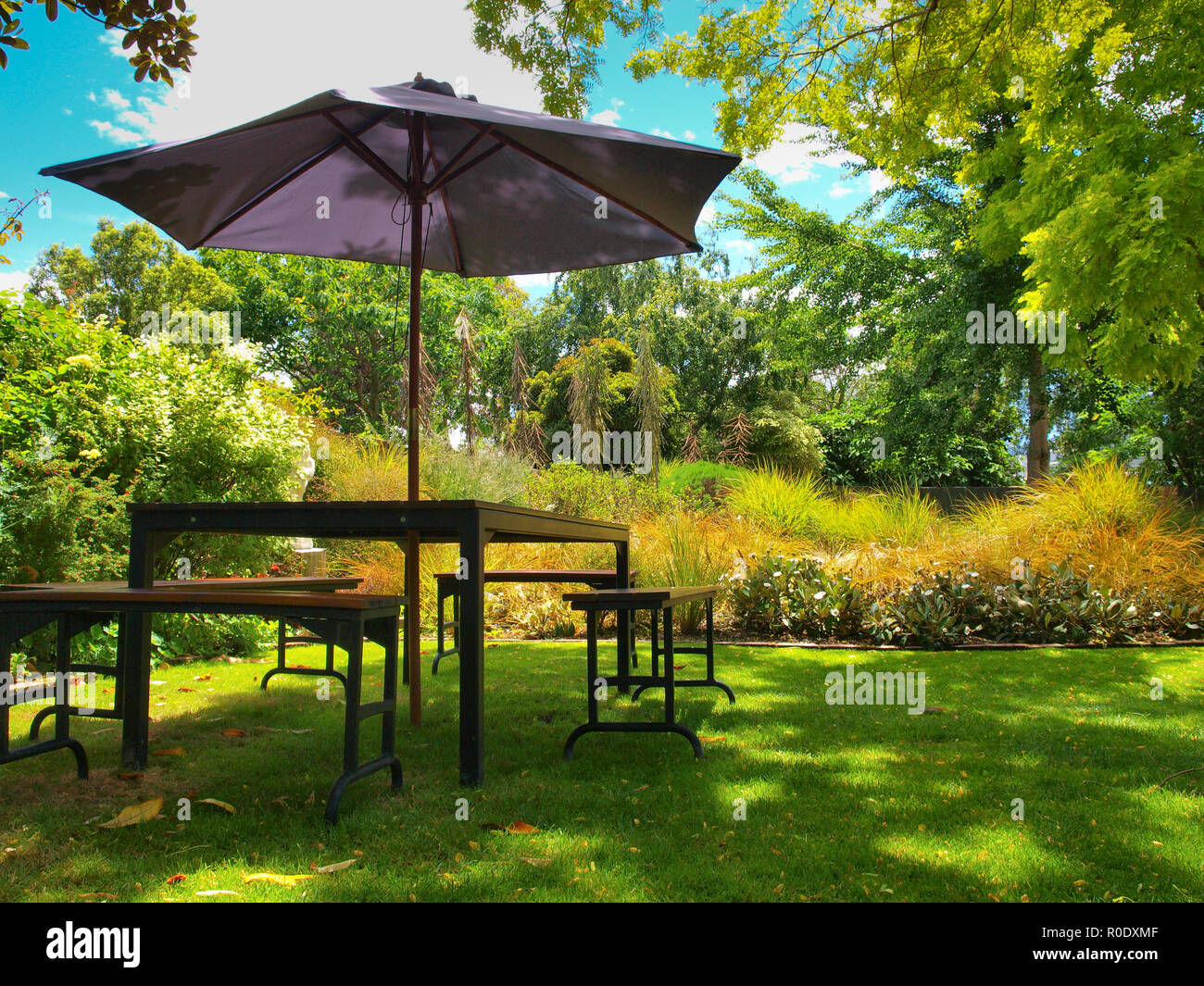 Esstisch mit Stühlen und Sonnenschirm im Schatten in einem üppigen Garten Stockfoto