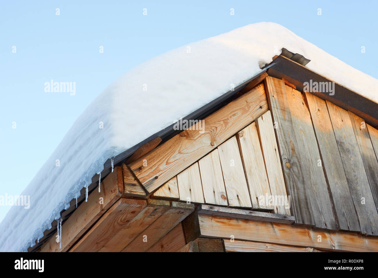 Dach der rustikalen hölzernen Gebäuden mit Schnee gegen den blauen Himmel in den Strahlen der untergehenden Sonne abgedeckt. Ansicht von unten Stockfoto