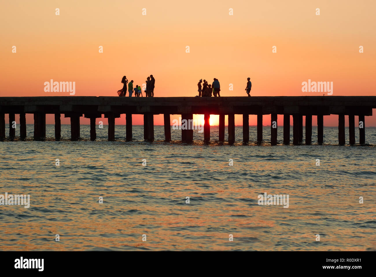 Gruppen von Menschen an der alten Pier genießen Sie den herrlichen Sonnenuntergang über der Küste des Schwarzen Meeres in der Republik Krim, Ukraine Stockfoto