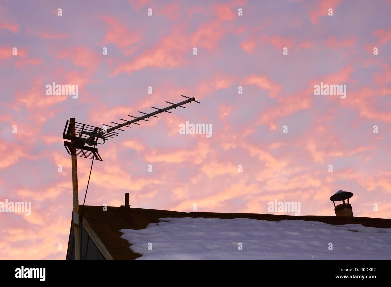 Fernsehen Antenne über den schneebedeckten Dach des alten Hauses gegen rötlich bewölkter Himmel am Abend Zeit Stockfoto