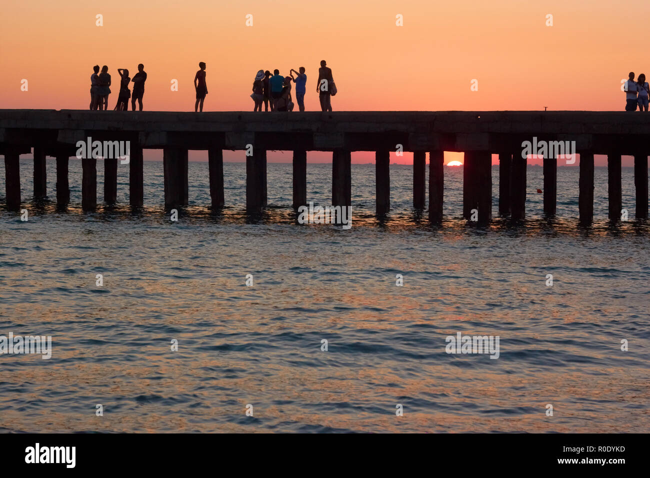 Gruppen von Menschen an der alten Pier sind fotografiert und bewundern Sie den wunderschönen Sonnenuntergang über der Küste des Schwarzen Meeres in der Republik Krim, Ukraine Stockfoto