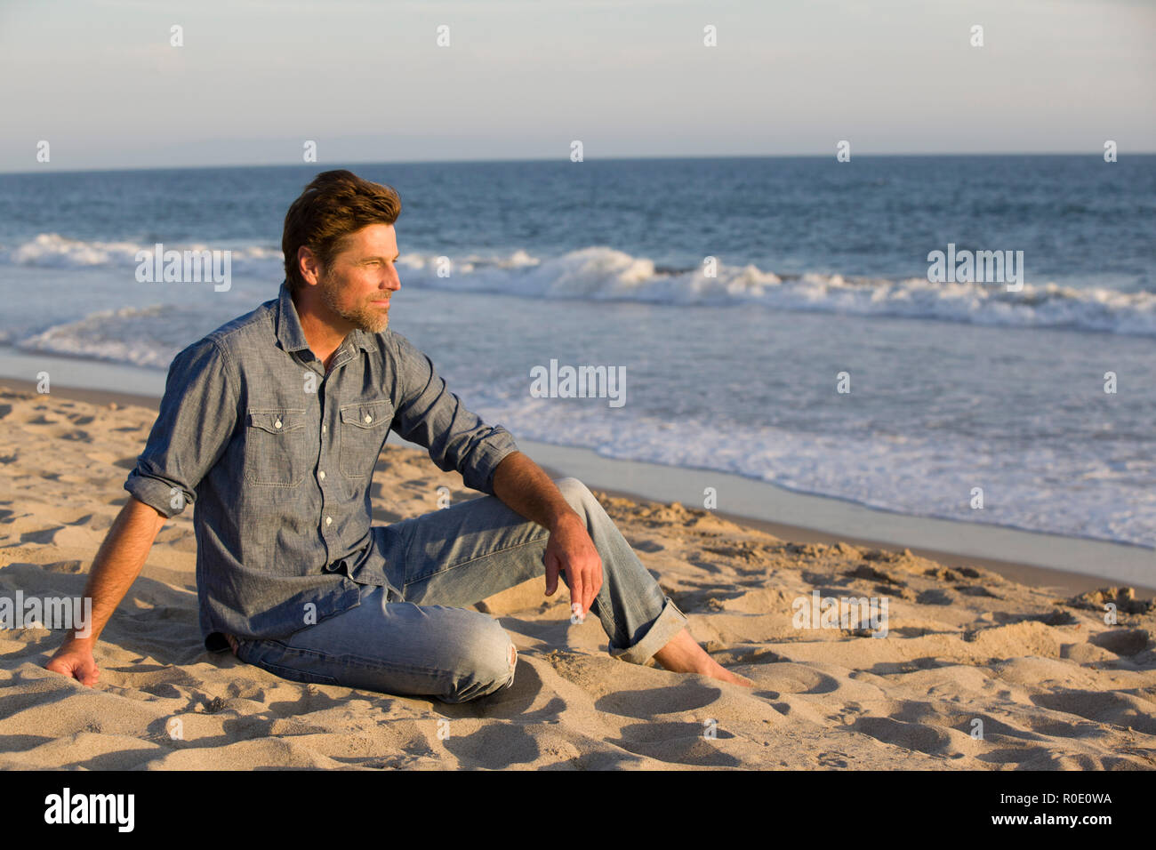 Kontemplative Mid-Adult Mann sitzt auf Sandstrand Stockfoto