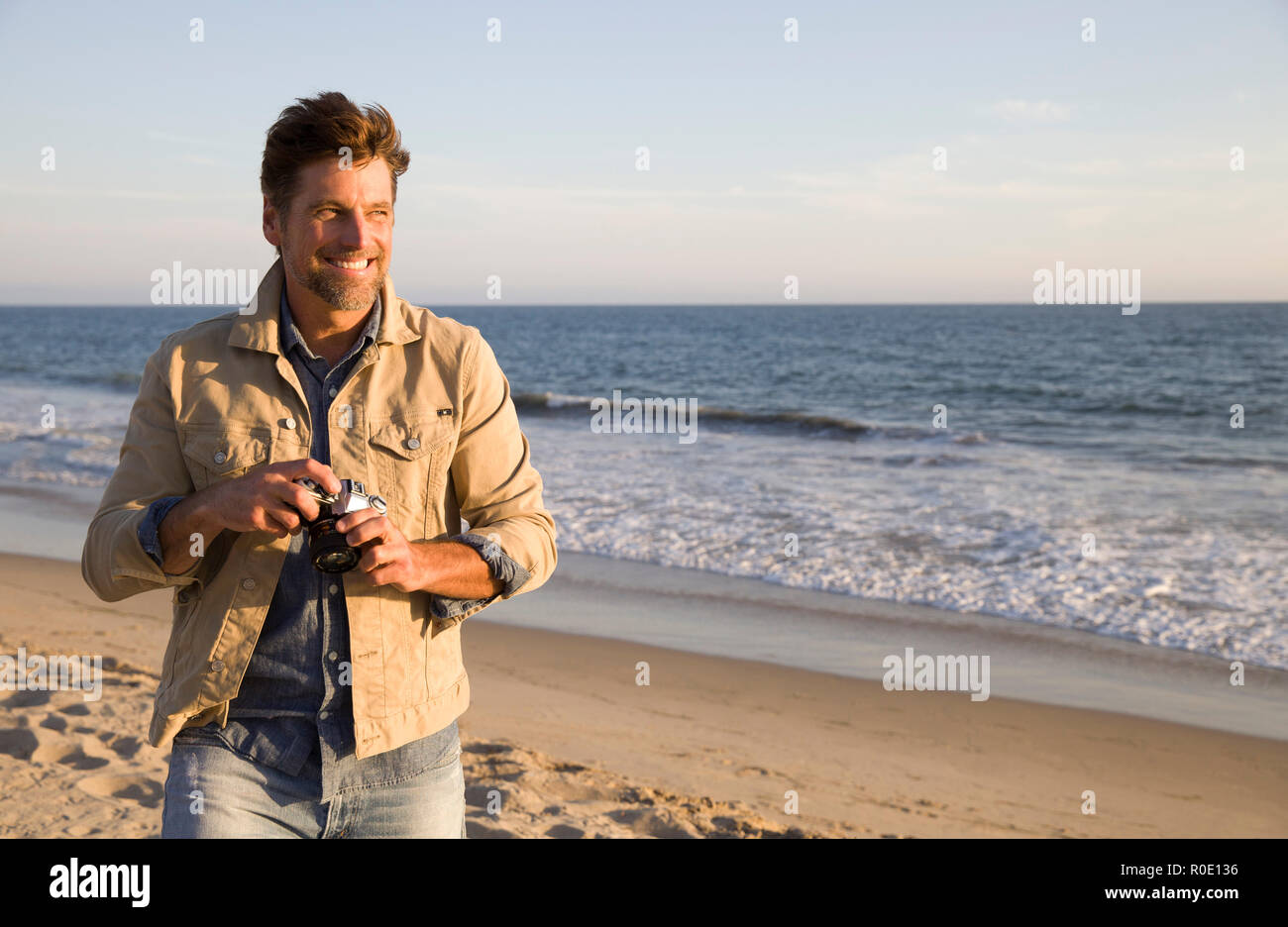 Halber Baulänge Portrait von lächelnden Mid-Adult Mann mit Kamera am Strand Stockfoto