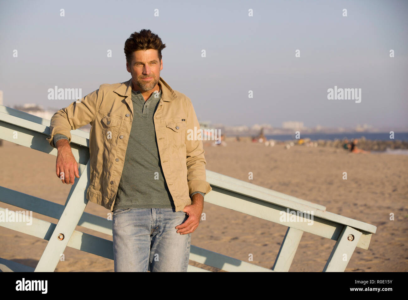 Drei viertel länge Portrait von Mid-Adult Mann in Freizeitkleidung lehnte sich gegen Geländer am Strand Stockfoto