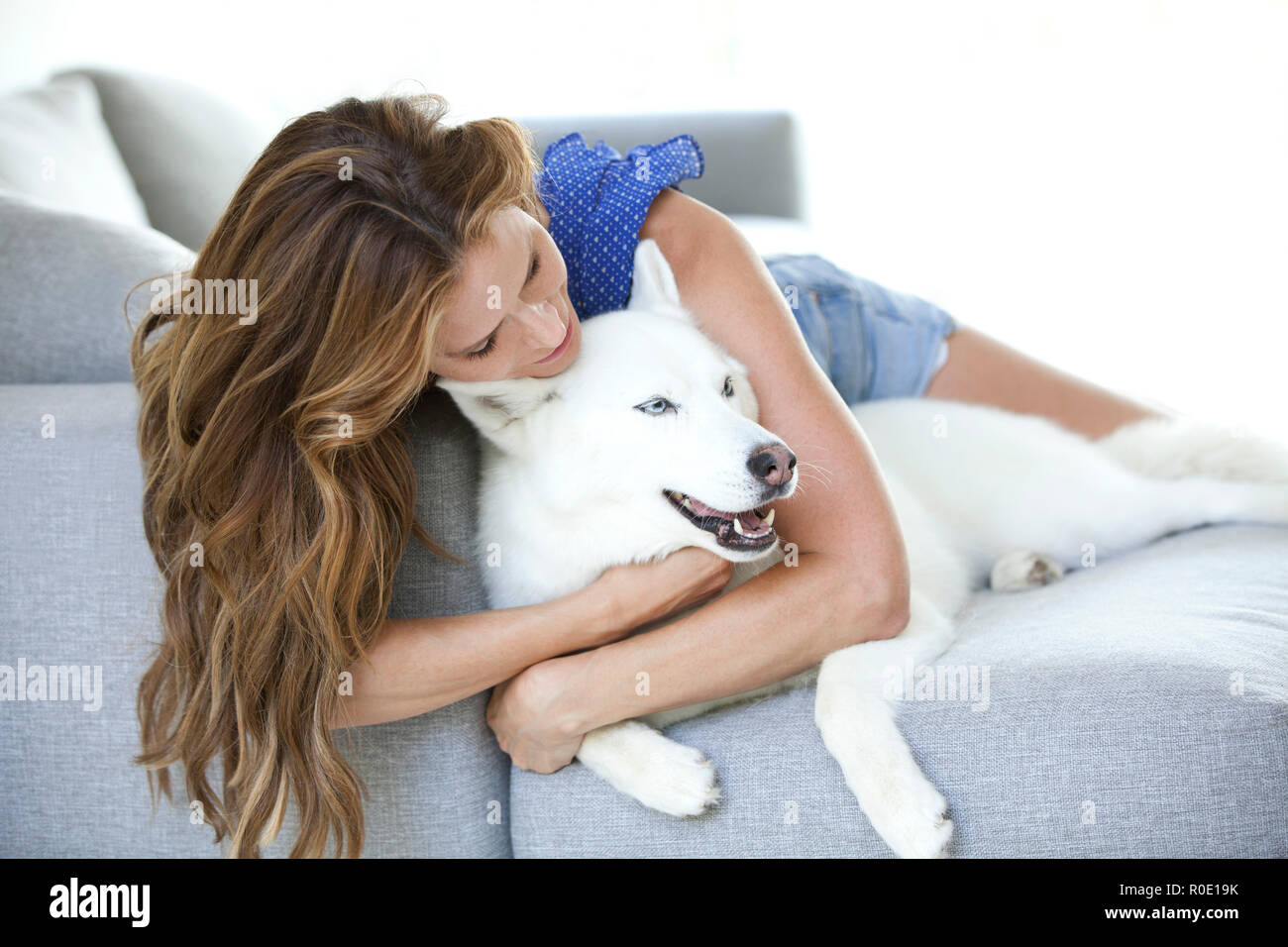 Mid-Adult Frau umarmen weißer Hund auf Sofa Stockfoto