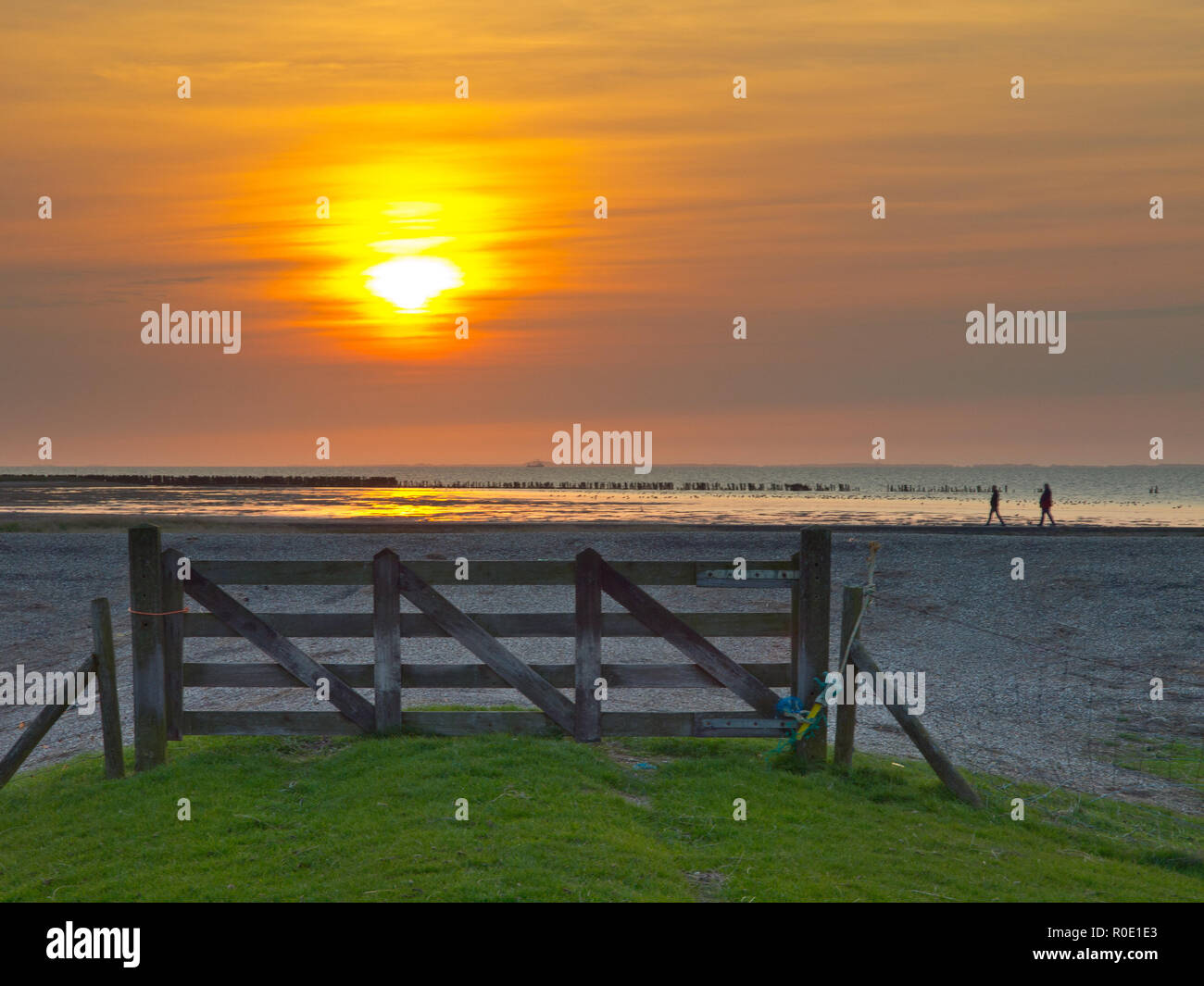Zonsondergang boven de Waddenzee vanachter een hek bij Paesens kammerforst. Twee mensen Ondertussen lopen Langs Stockfoto