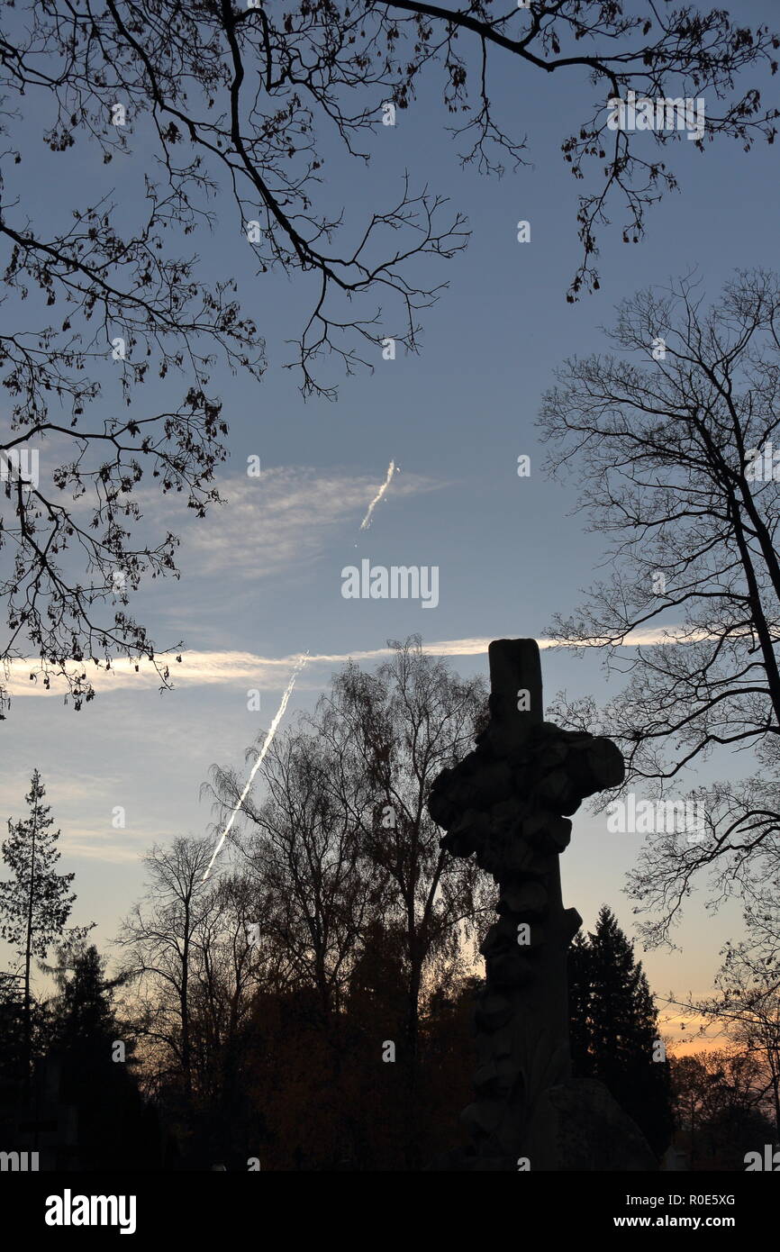 Jet fuel Wanderwege auf den Abendhimmel mit Silhouette der skulpturalen Grabstein Kreuz im Vordergrund. Stockfoto