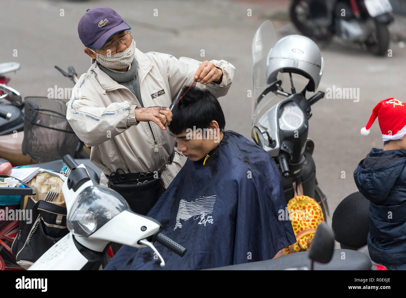 HANOI, VIETNAM, Dezember 15, 2014: ein Nomade Friseur ist außerhalb der in der Stadt, seine Kunden auf seinem Motorrad in Hanoi, Vietnam sitzt. Stockfoto