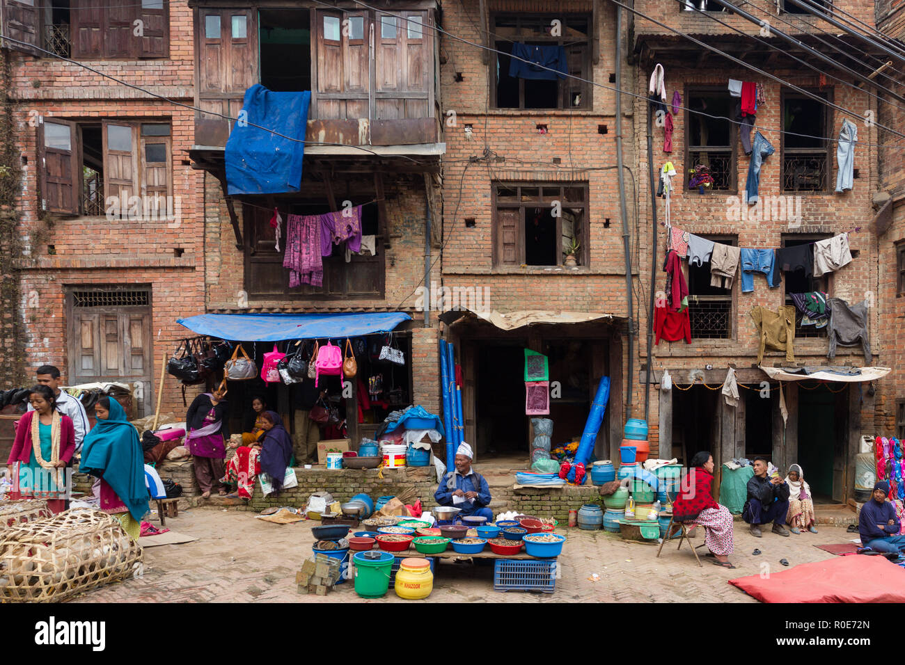 BHAKTAPUR, Nepal, November 25, 2010: Blick auf einen kleinen Marktplatz mit Kleidung und Essen Verkäufer vor einem traditionellen alten Gebäude in Bhaktapur Stockfoto