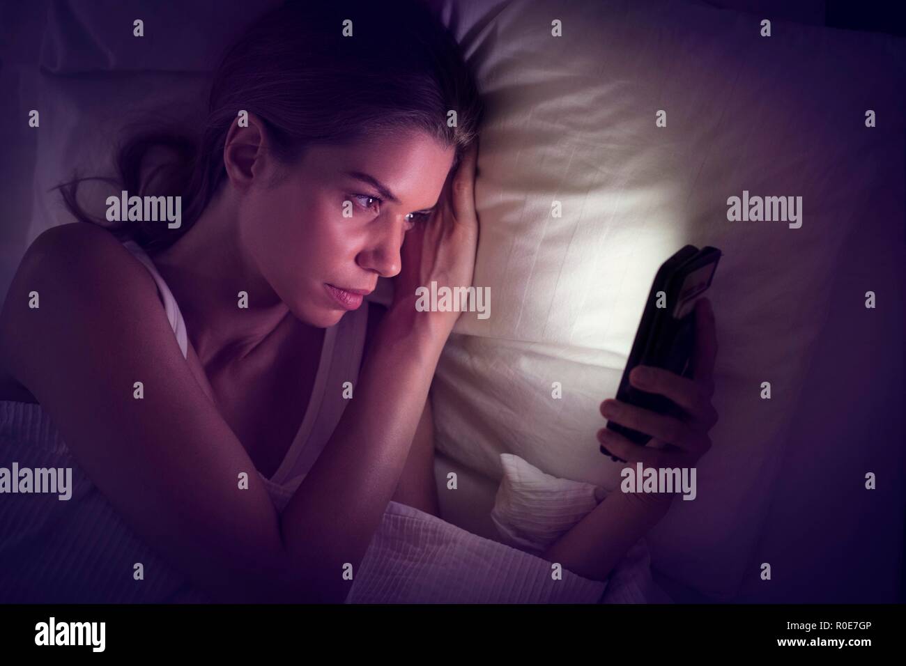 Junge Frau von Smartphone im Bett suchen. Stockfoto