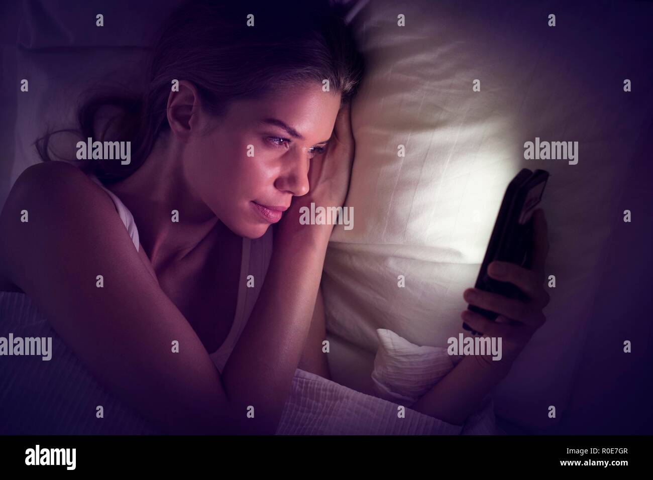 Junge Frau von Smartphone im Bett suchen. Stockfoto