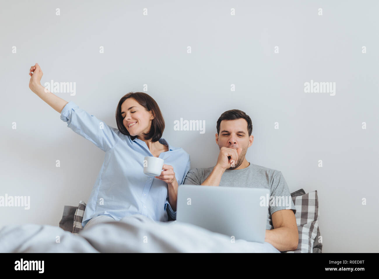 Froh Dass Weibliche Erstreckt Sich Im Bett Trinken Heissen Kaffee Und Ihr Mann Arbeitet Die Ganze Nacht Am Laptop Gahnt Will Schlafen Verbringen Zeit Miteinander Stockfotografie Alamy