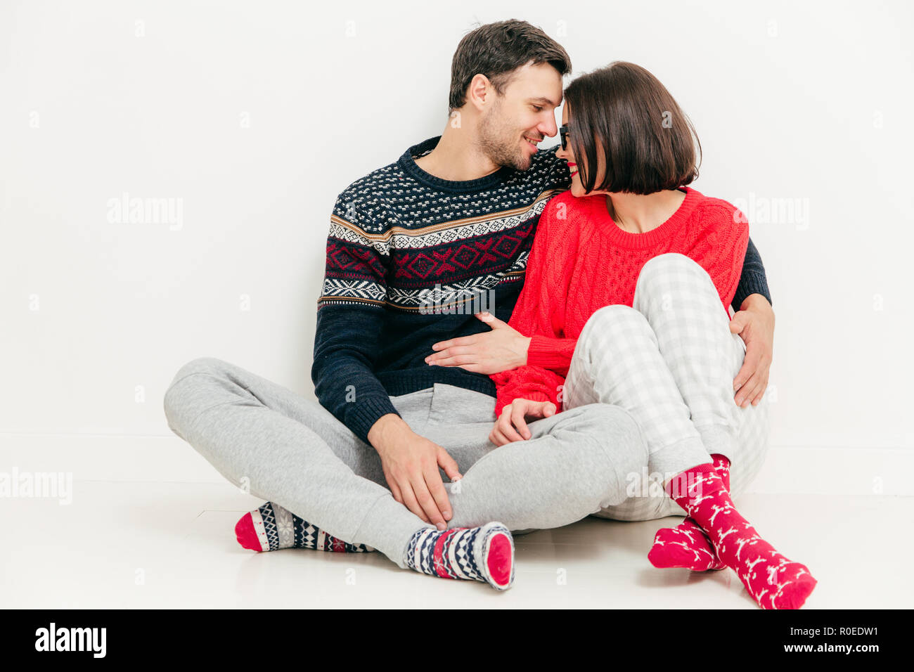 Foto von romantisches Paar in Liebe sitzen auf weißen Boden gekreuzten Beinen, blicke mit großer Liebe, umarmen und genießen Sie Zweisamkeit, Auf der whi isoliert Stockfoto