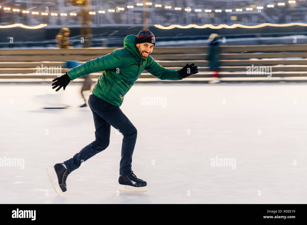 Der freundliche Mann hat Spaß im Freien, Schlittschuhen auf dem Eis ring, genießt dieser Winter Aktivität, bewegt sich aktiv, versucht, Balance zu halten, die gut ausgebildet, Loo Stockfoto