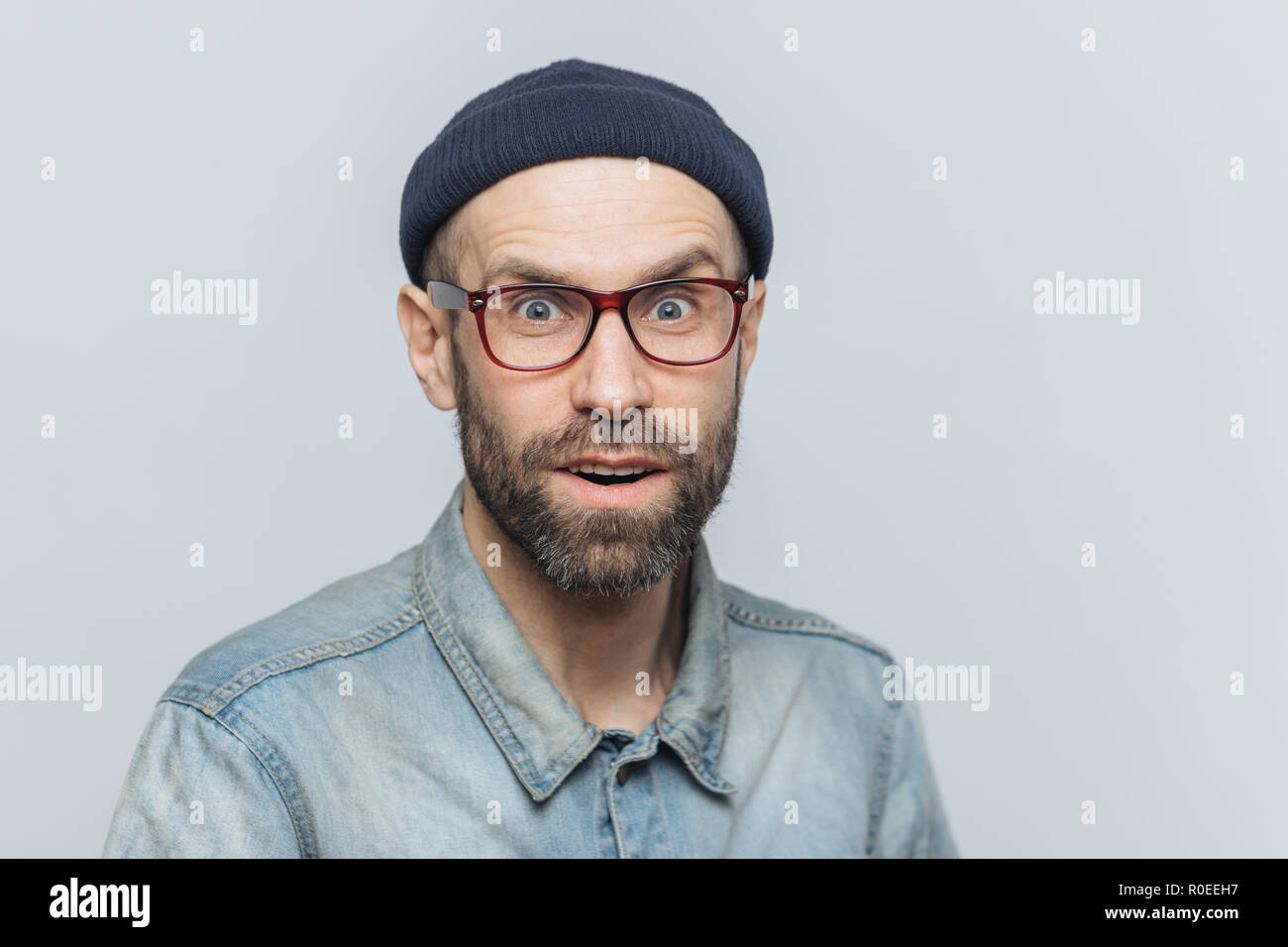 Headshot von gut aussehenden unrasierten Mann mit blauen Augen, blickt mit überrascht Ausdruck in Kamera, fühlt sich aufgeregt und mit neuesten Nachrichten schockiert, stellt ein Stockfoto