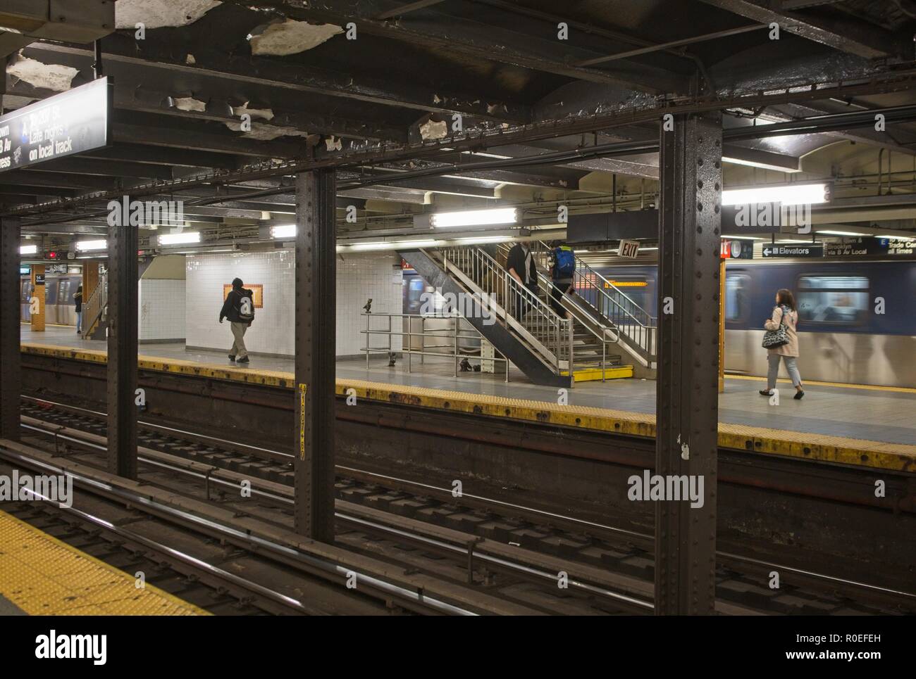 Eine Station in der New Yorker U-Bahn mit Passagieren beim Warten auf den nächsten Zug. Ein fahrender Zug passiert den Bahnhof im Hintergrund. Stockfoto