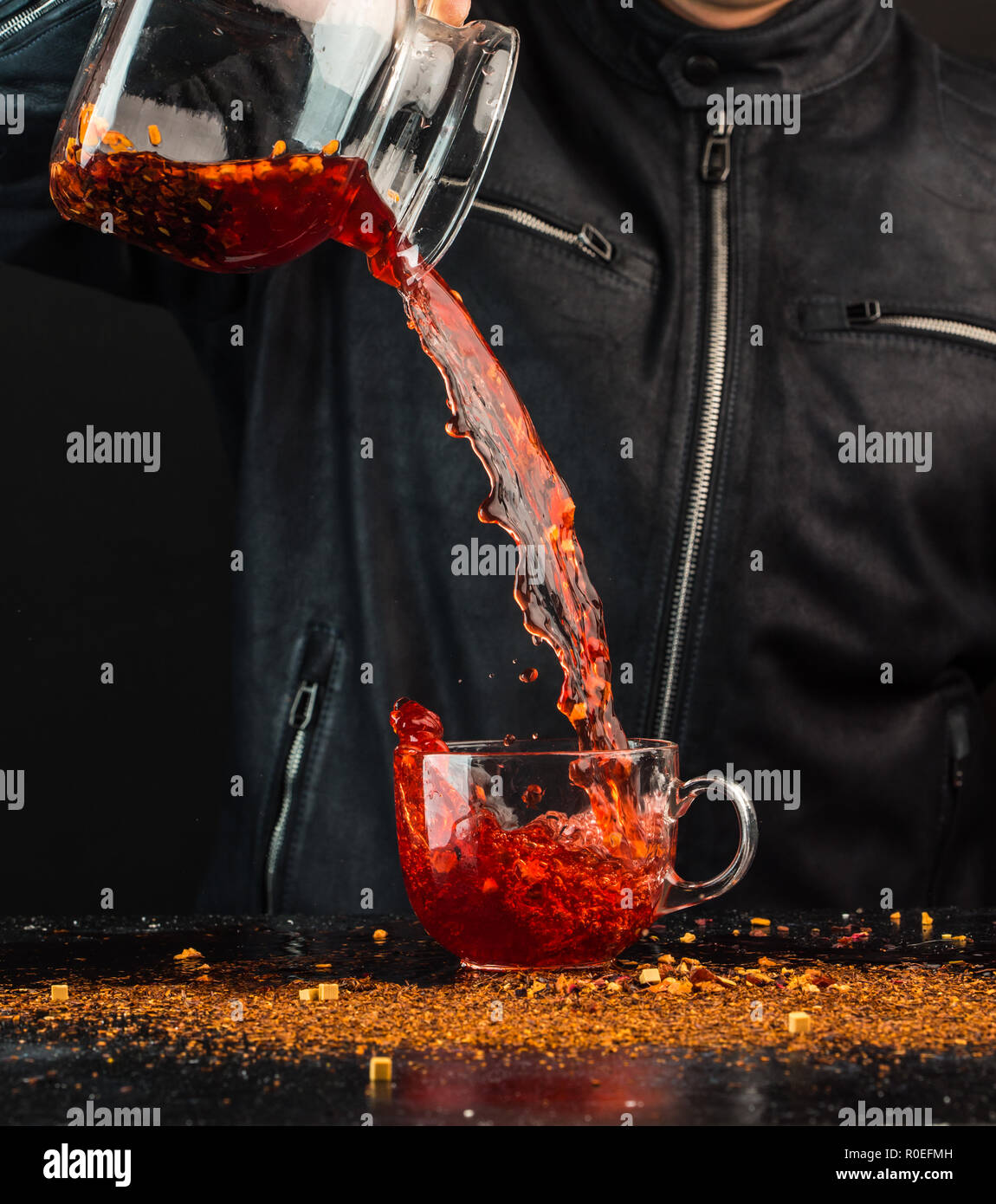 Ein Mann gießt ein Getränk aus einer Kanne in ein Glas Schale, können Sie sehen, Tropfen und Spritzwasser Stockfoto