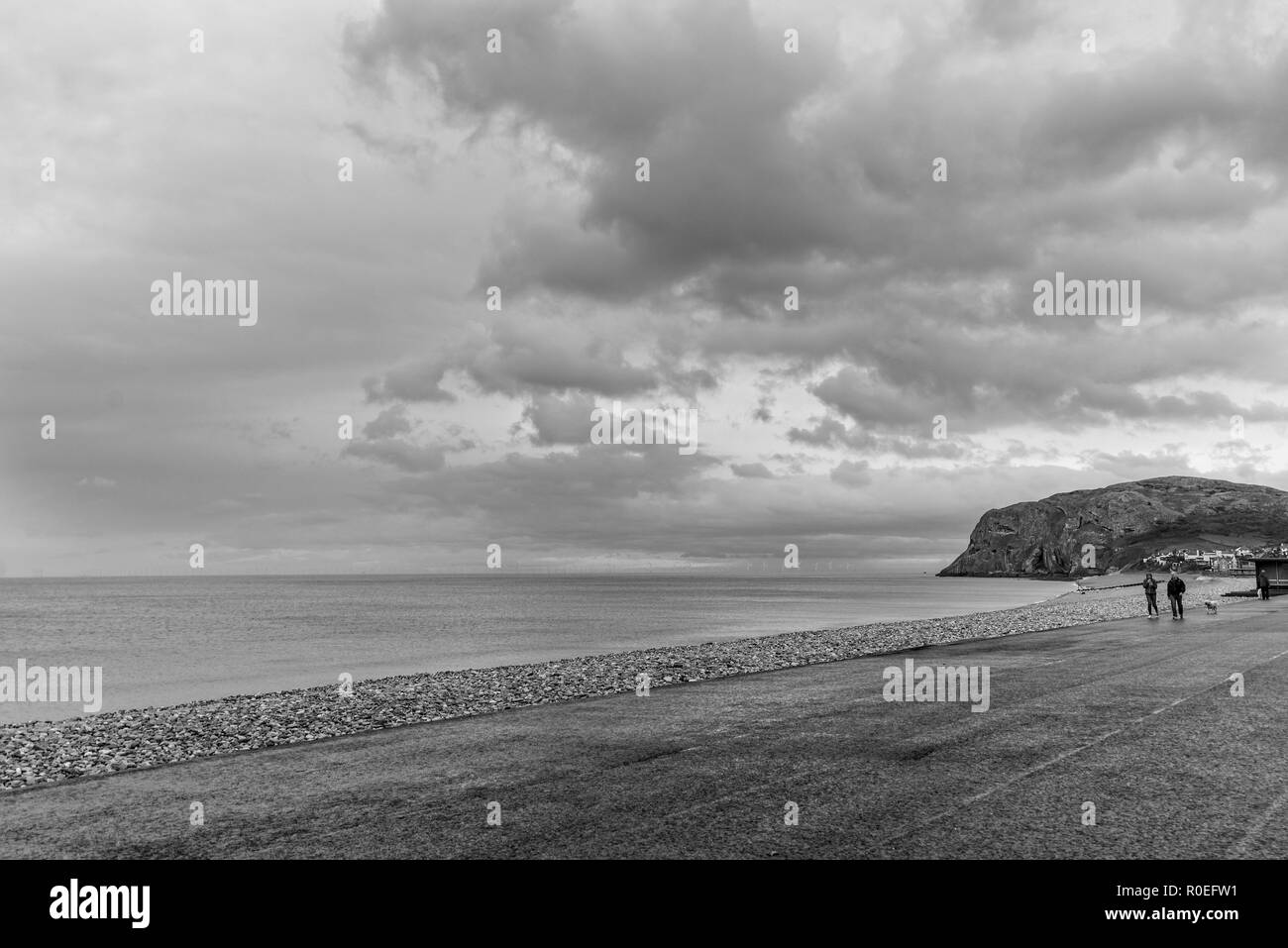 Ein Blick auf die Küstenlinie von Llandudno am frühen Morgen mit Menschen zu Fuß. Die Little Orme ist in der Ferne und ein dramatischer Himmel ist Overhead. Stockfoto