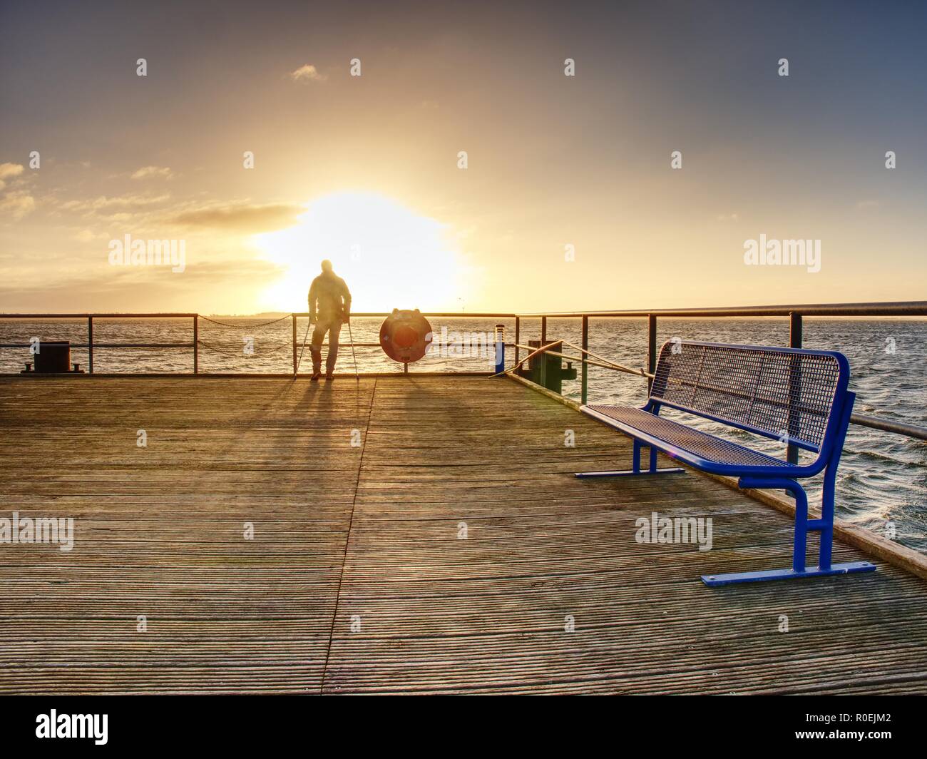 Mann Wanderer mit Rucksack stand alone und romantischen farbenfrohen Sonnenaufgang über hölzerne Seebrücke Stockfoto