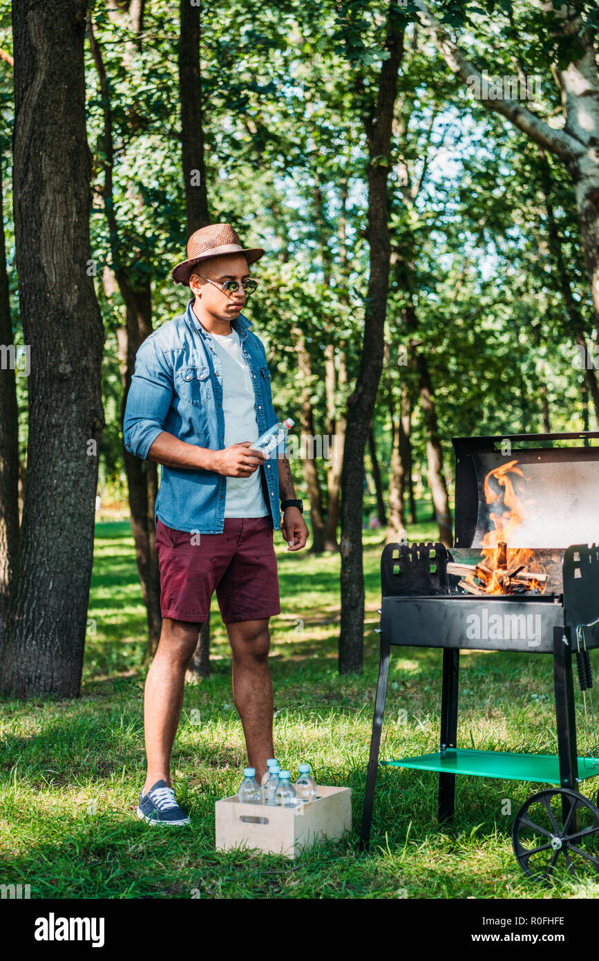 Afrikanische amerikanische Mann in Sonnenbrille und Hut Einstellung Brand am Grill im Park Stockfoto