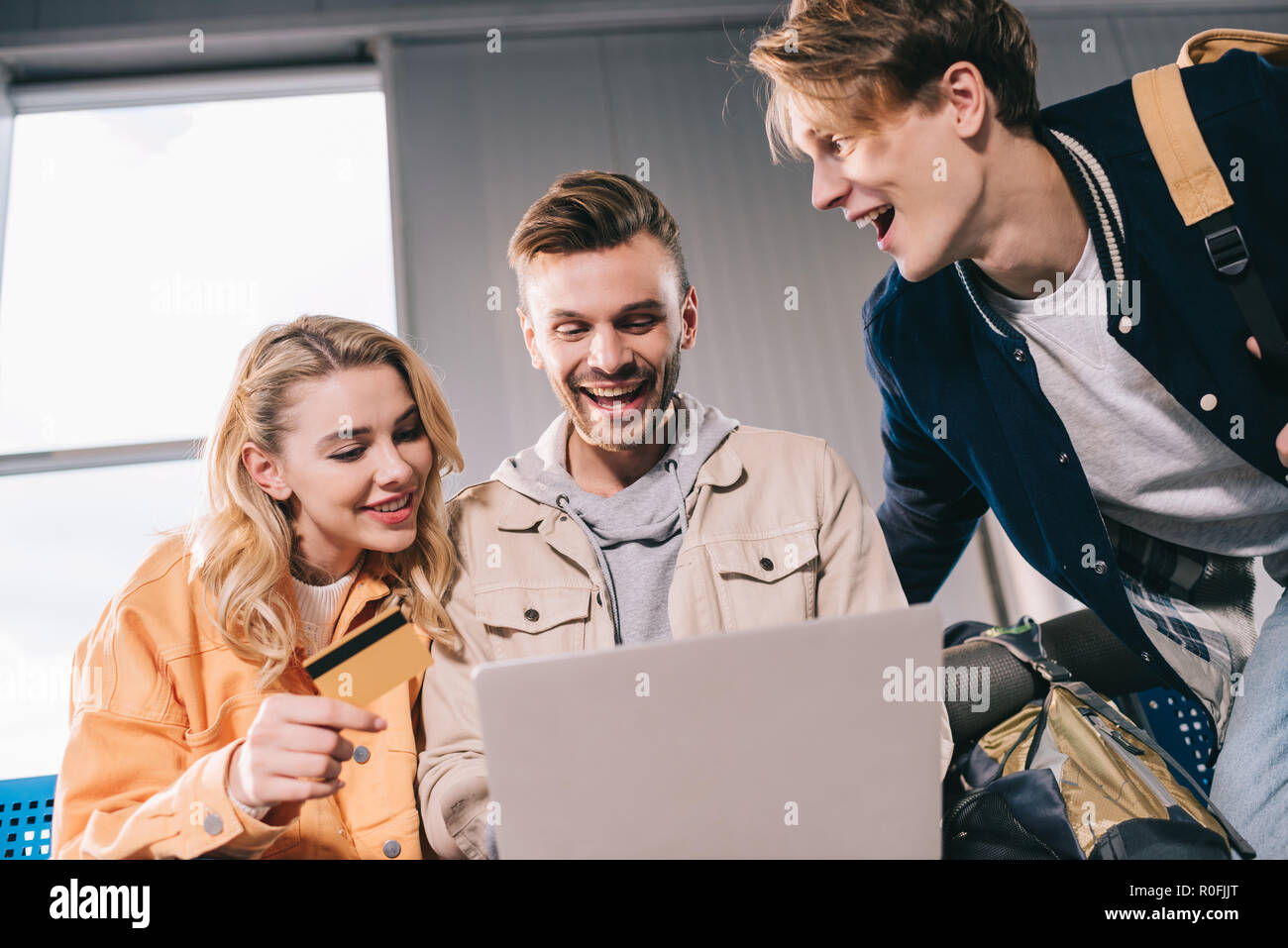 Fröhliche Freunde mit Kreditkarte mit Laptop im Flughafen Stockfoto