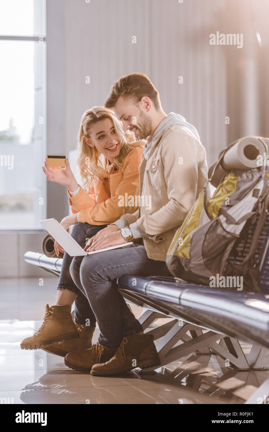 Lächelnde Mädchen holding Kreditkarte während Mann mit Laptop im Flughafen Terminal Stockfoto