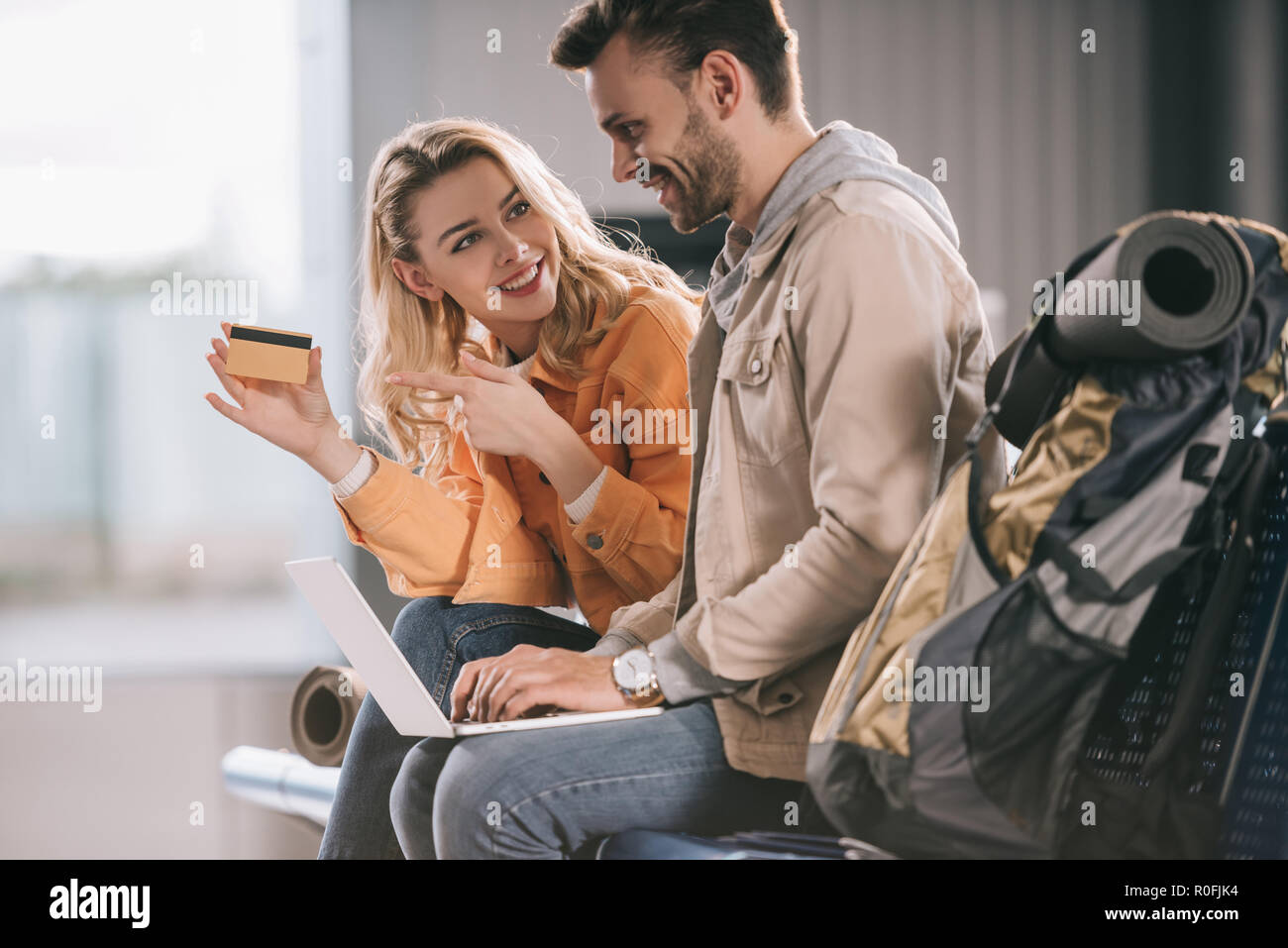 Lächelnde Mädchen zeigte mit dem Finger auf Kreditkarte und Mann mit Laptop im Flughafen Stockfoto