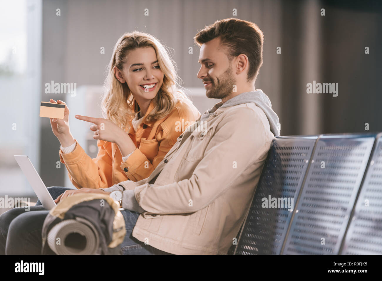 Lächelnde junge Frau zeigt mit dem Finger auf Kreditkarte und Mann mit Laptop im Flughafen Stockfoto