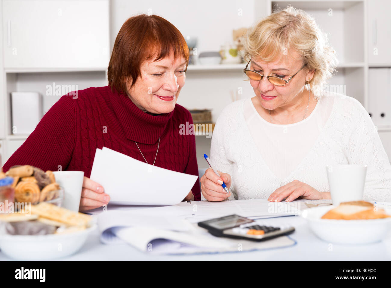Zwei positive reife Frauen, die Papiere beim Sitzen auf Küche Stockfoto