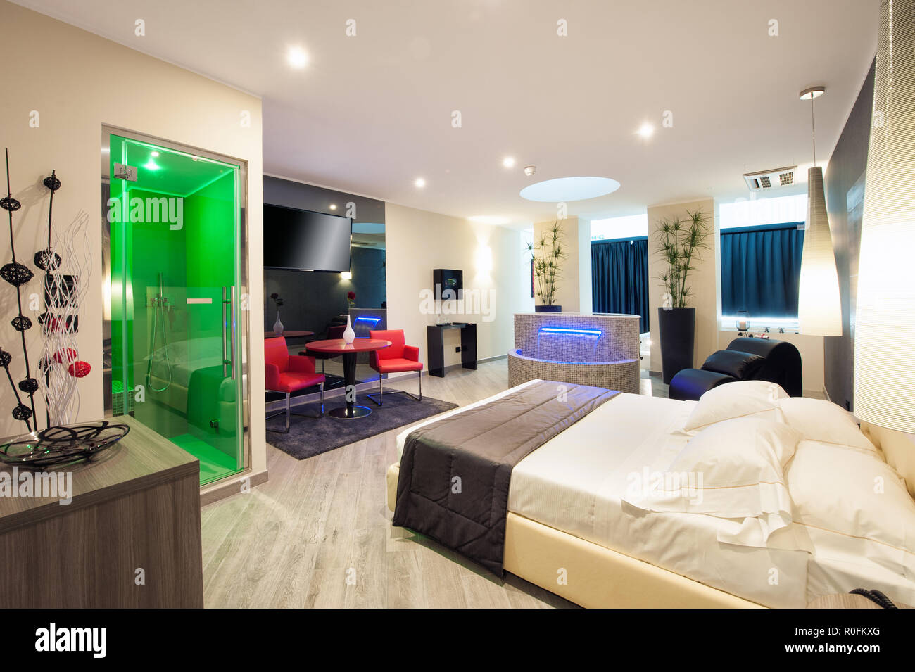 Double en-suite Motel Schlafzimmer mit Dusche, komfortablen Doppelbett und Sitzecke in neutralem Dekor bei Nacht beleuchtet Stockfoto