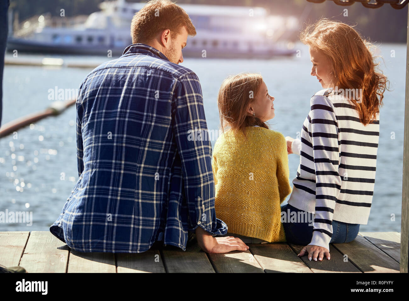 Ansicht der Rückseite des Familie sitzen auf Pier im Herbst Tag. Herbst Family Portrait Stockfoto