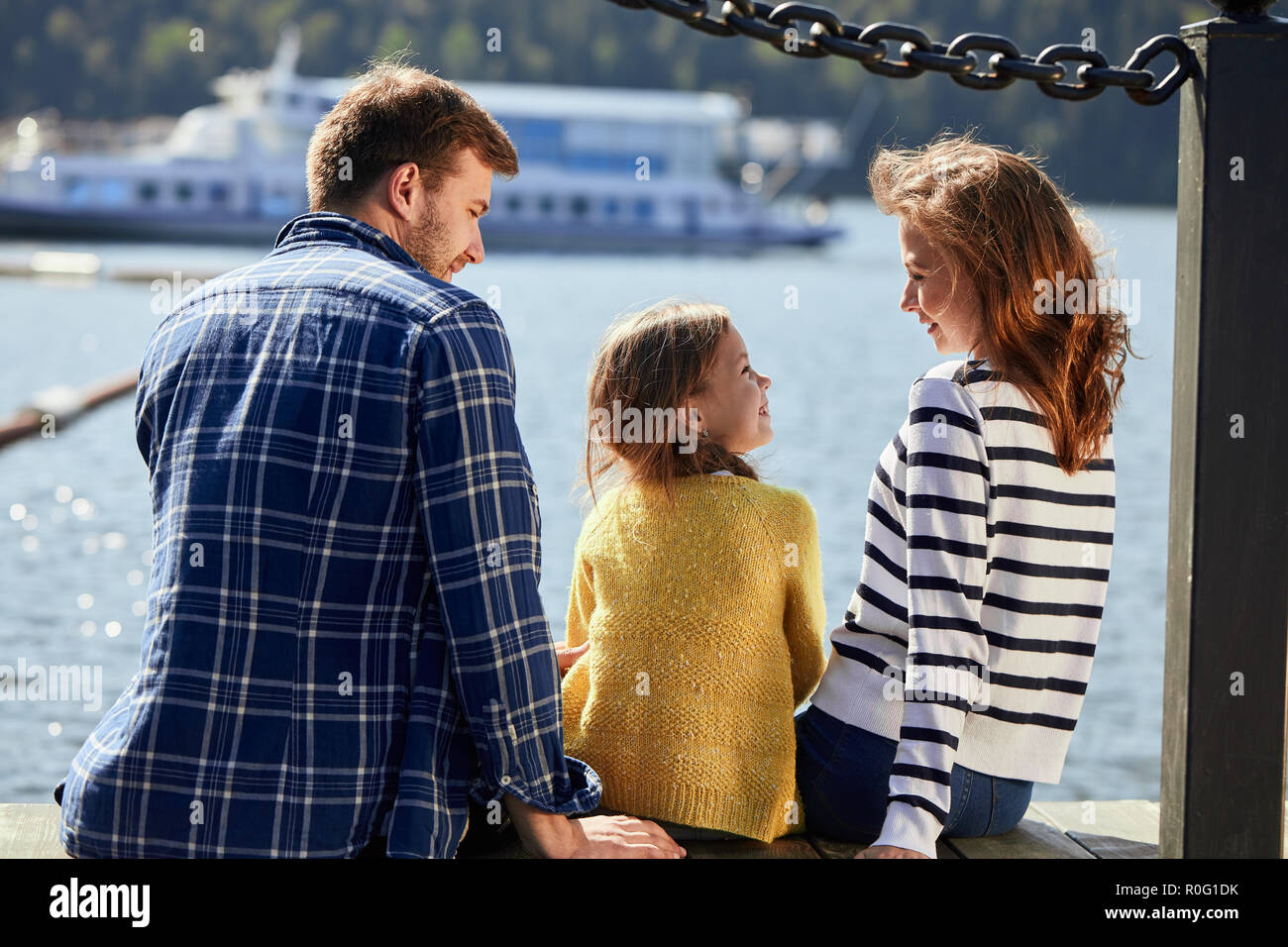 Ansicht der Rückseite des Familie sitzen auf Pier im Herbst Tag. Herbst Family Portrait Stockfoto