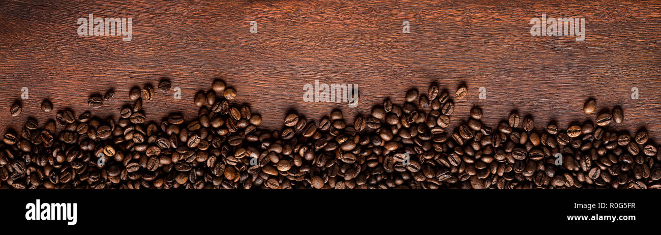 Frisch geröstete Kaffeebohnen auf natürliche dunkle Eiche Holz panorama breiten hölzernen closeup Makro Hintergrund Stockfoto