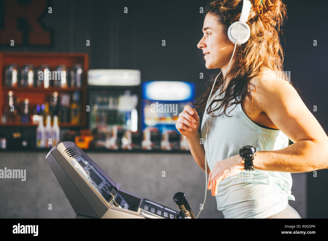 Thema ist Sport und Musik. Eine schöne aufgeblasen Frau läuft im  Fitnessstudio auf dem Laufband. Auf dem Kopf sind große weiße Kopfhörer,  das Mädchen Musik hört, d Stockfotografie - Alamy