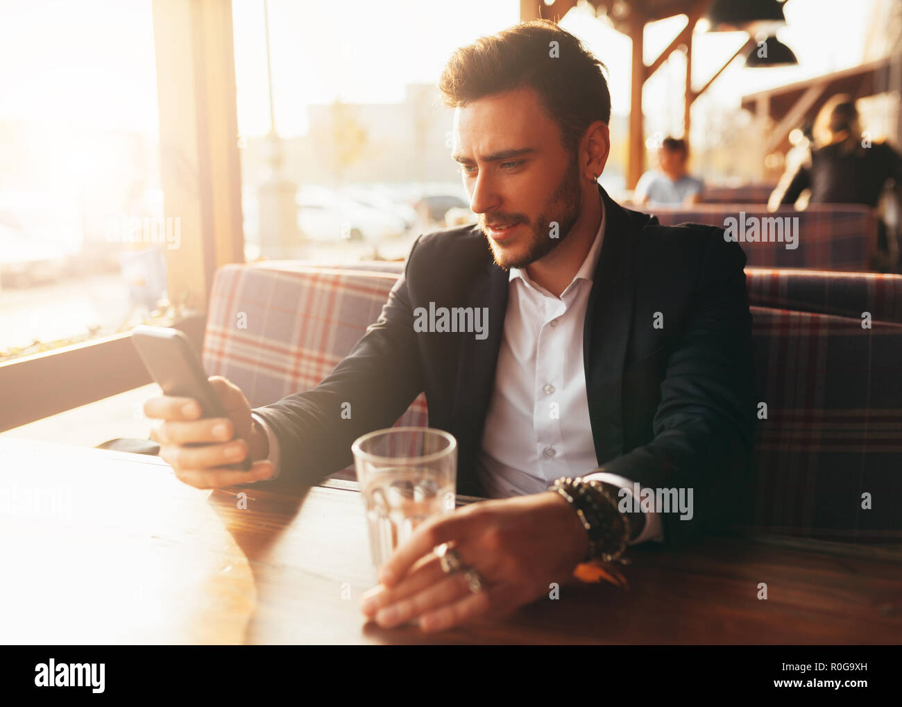 Tausendjährige Geschäftsmann in einem Cafe sitzen an einem Tisch und auf den Bildschirm seines Handys. Junge erfolgreiche stilvollen Mann ruht in einem Sommer Cafe Stockfoto
