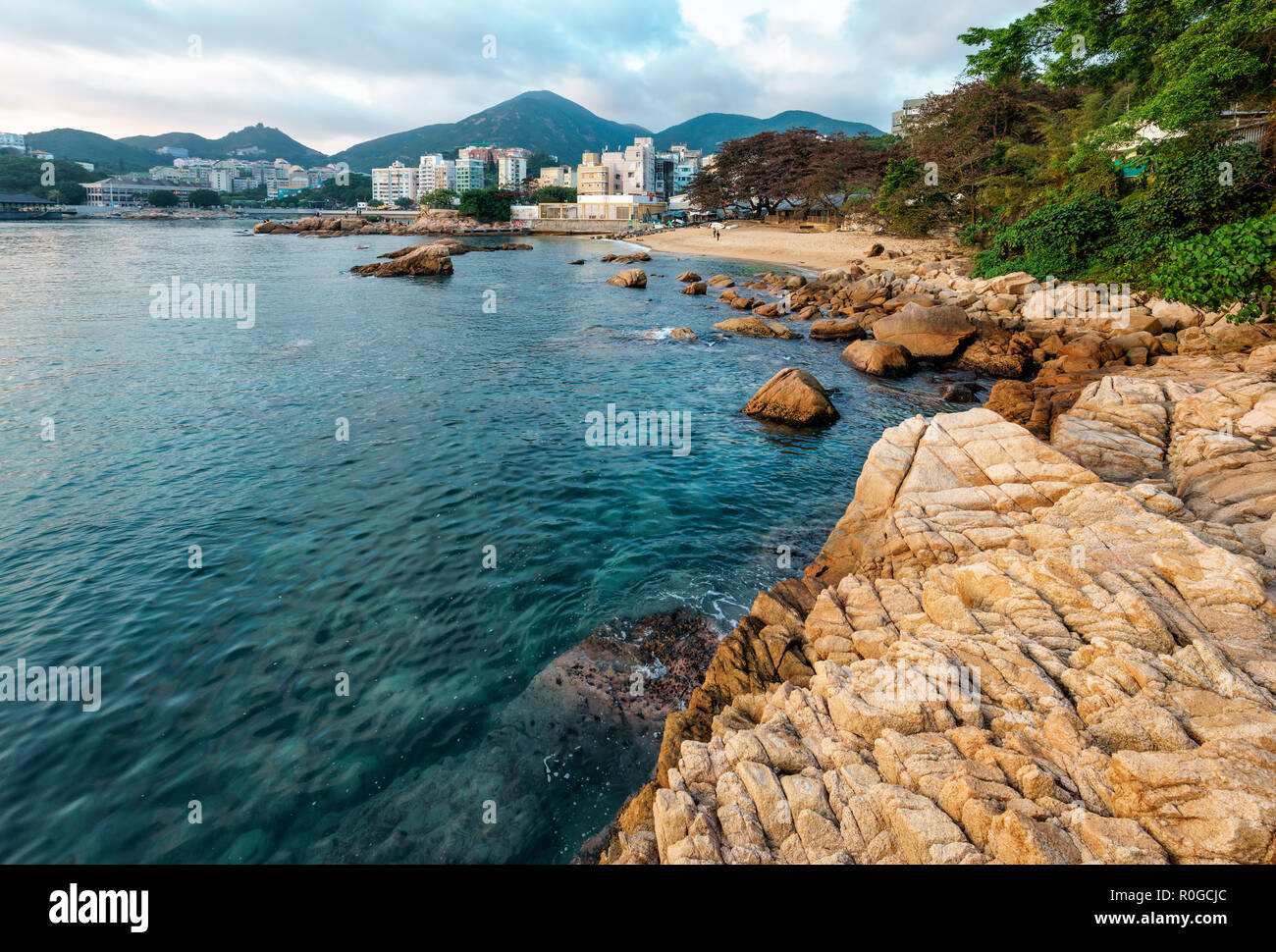 Felsige Küste von Stanley Bay in Hongkong. Landschaftlich schöne Landschaft mit Wasser, Berge, Felsen, Gebäude und bewölkter Himmel Stockfoto