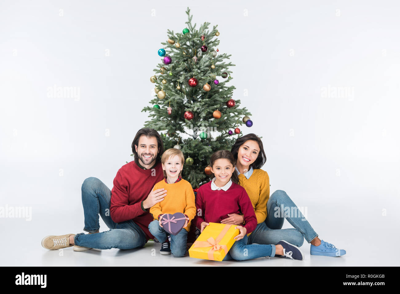 Glückliche Familie sitzt in der Nähe der Weihnachtsbaum mit Geschenken isoliert auf weißem Stockfoto