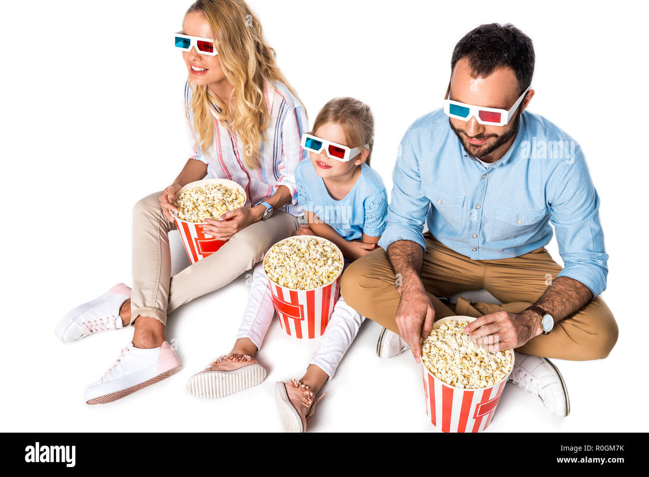 Familie mit Popcorn und 3D-Brille sitzen auf White Cube isoliert auf weißem Stockfoto