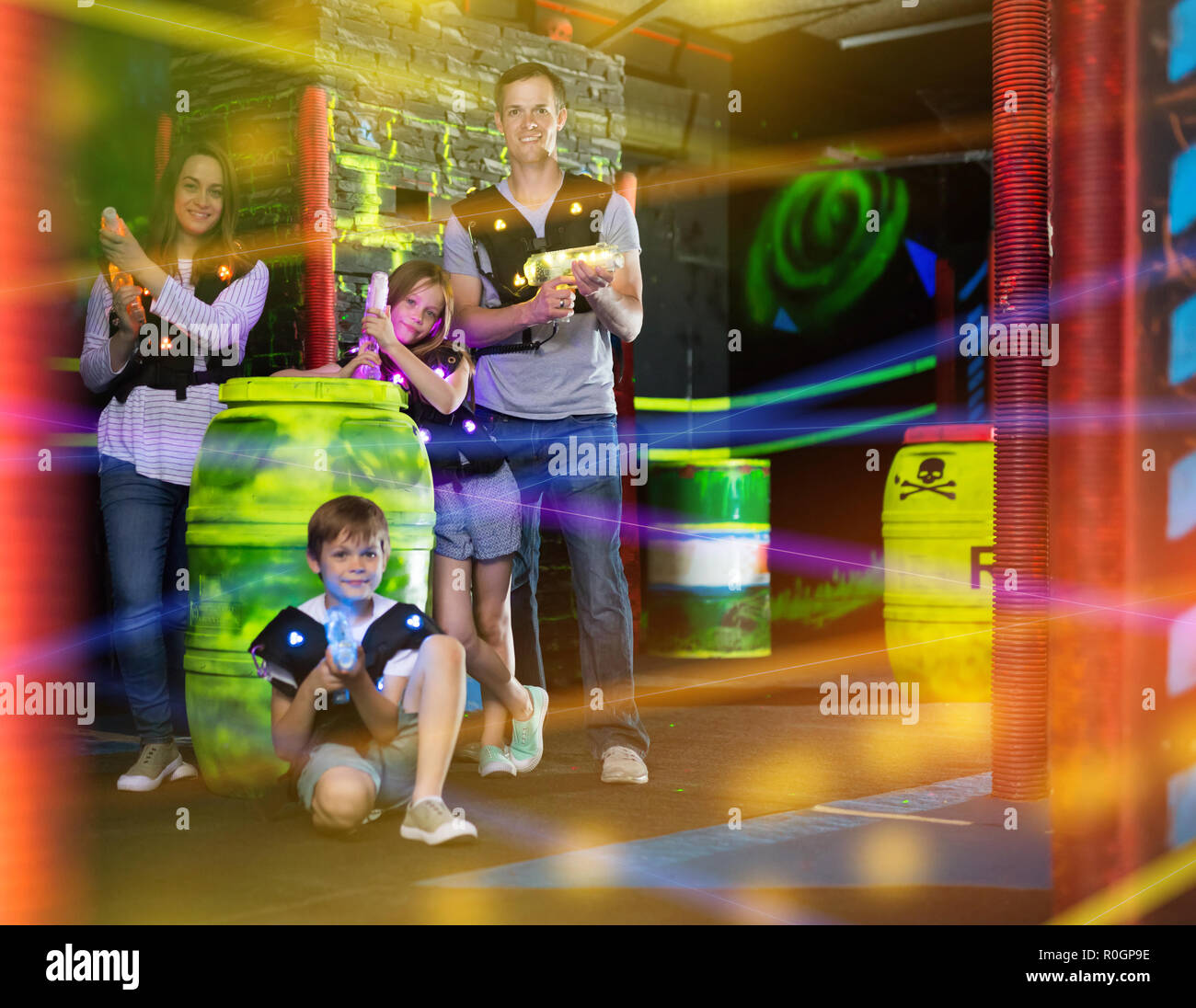 Portrait von Happy Kids und ihre Eltern mit Laserwaffen in farbigen Balken während der Laser tag spiel in dunklen Zimmer Stockfoto