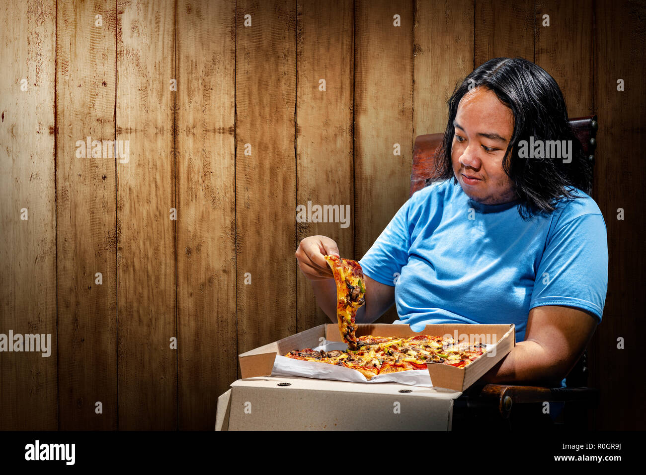 Jungen asiatischen Fat man essen Pizza auf einen Stuhl. Fat Man Diät Konzept Stockfoto