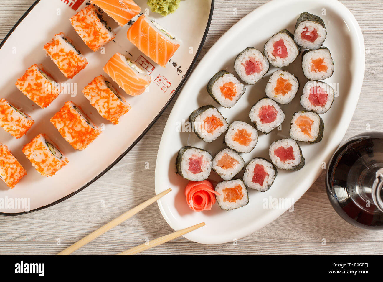 Verschiedene sushi Rollen mit Reis, Gemüse, Fisch und Meeresfrüchte auf keramischen Platten und Glasflasche mit Sojasauce auf hölzernen Schreibtisch. Ansicht von oben Stockfoto